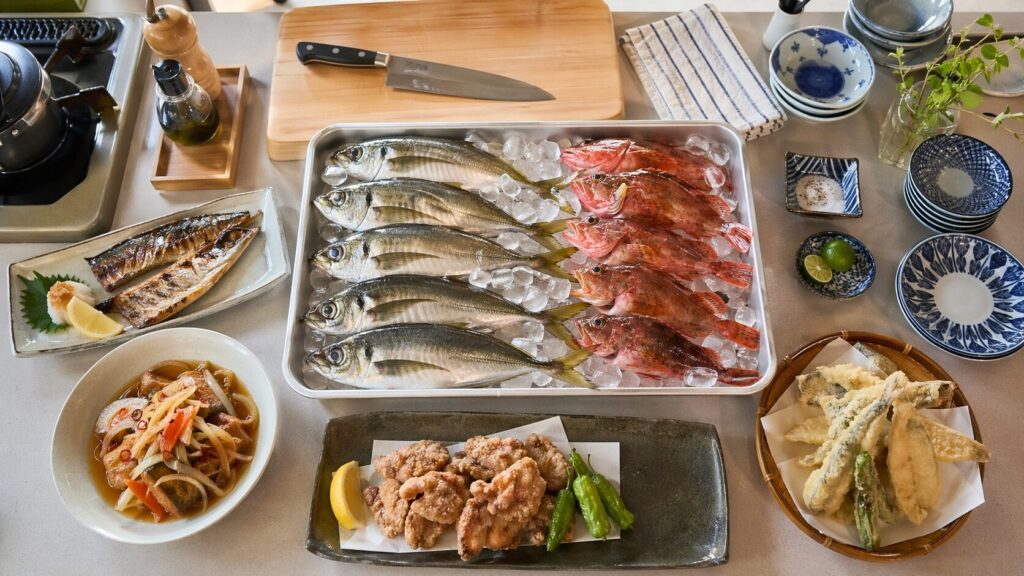キッチンカウンターに並ぶ釣りたてのアジとカサゴ・塩焼き・南蛮漬け・唐揚げ・天ぷらの完成料理・自炊の喜びが伝わるフードフォト